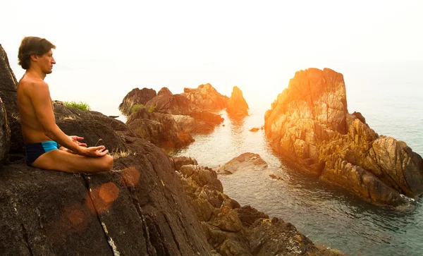 Man doing yoga exercise on the deserted wild stone sea beach at sunset