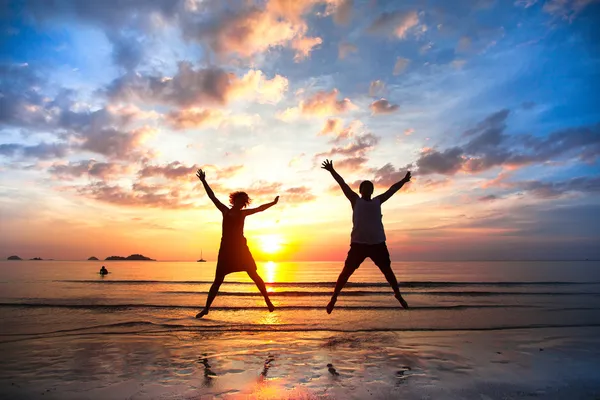 Young couple in a jump on the sea beach at sunset (concept of long-awaited vacation)