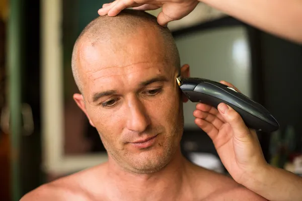 Hairdresser shaving man with hair trimmer.