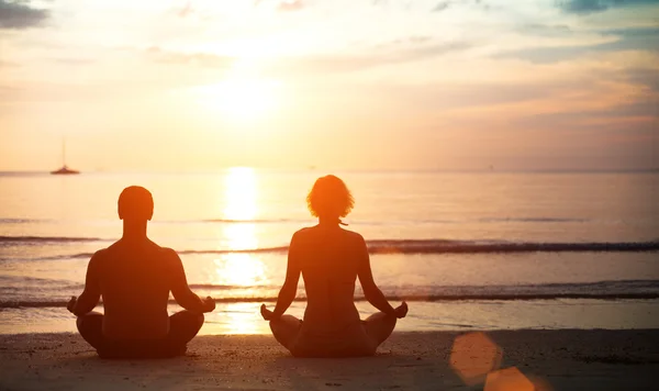 Young couple in a lotus position meditating on the beach at sunset.