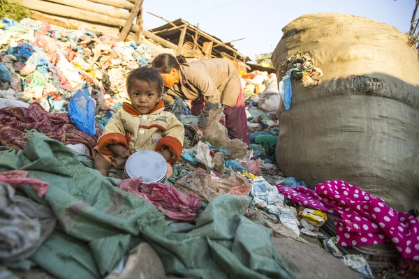 Unidentified child is sitting while her parents are working on dump
