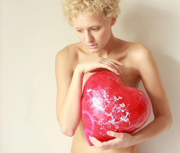 Young sexy girl holding a big toy red heart, in gentle tones