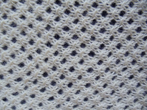 Close-up. Natural woolen handmade knitted fabric of an ivory colour with a seamless fishnet pattern on a dark blue background.