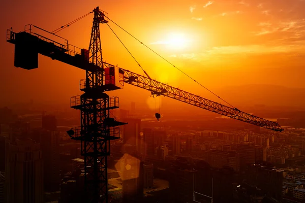 Industrial construction cranes and building silhouettes over sun at sunrise.