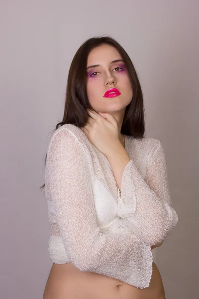 Studio emotional portrait of a beautiful young brunette woman with pink lips, wearing a white blouse
