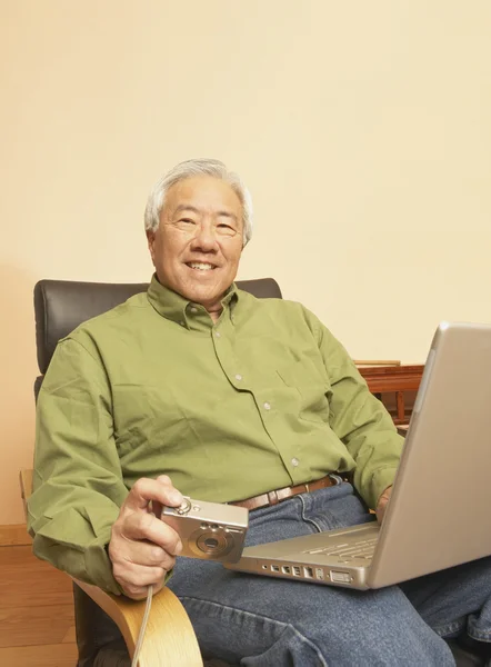 Senior Asian man with laptop and digital camera