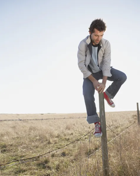 Young man climbing over barbed wire fence