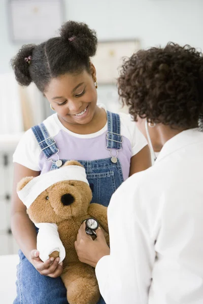 African American female doctor examining girl\'s teddy bear