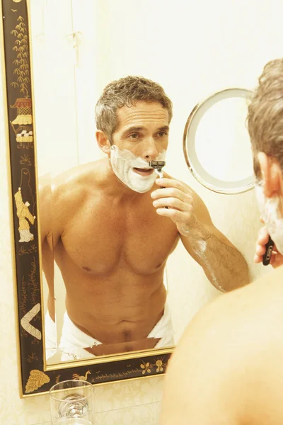 Middle-aged man shaving in mirror