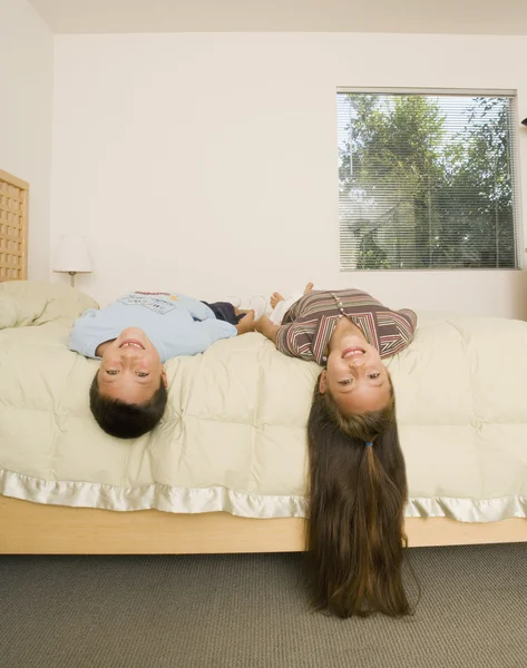 Asian brother and sister laying with heads off bed