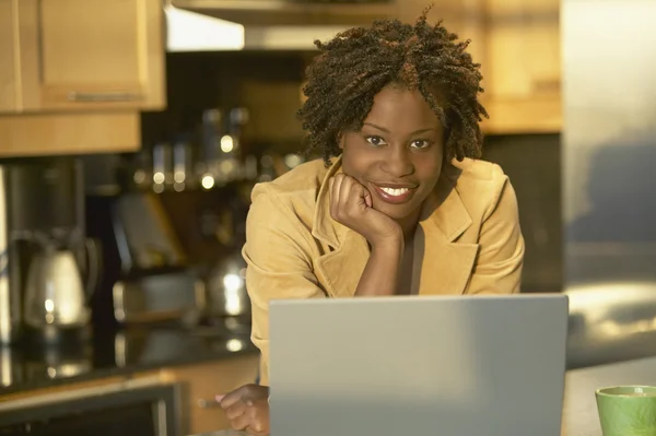 Young African woman in kitchen with laptop