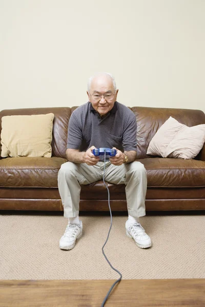 Elderly man sitting on couch playing video games