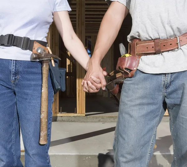 Couple holding hands and wearing tool belts