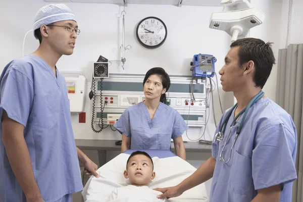 Asian boy in hospital bed with doctors talking