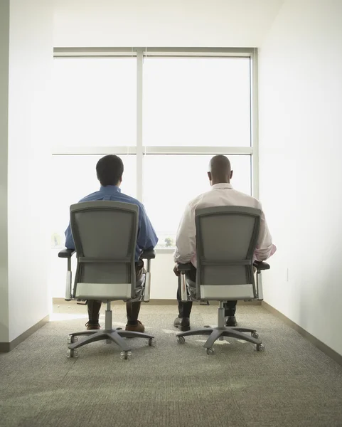 Businessmen sitting in swivel chairs in empty office space