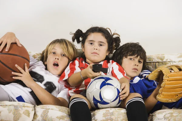 Group of children in sports gear watching television on the sofa