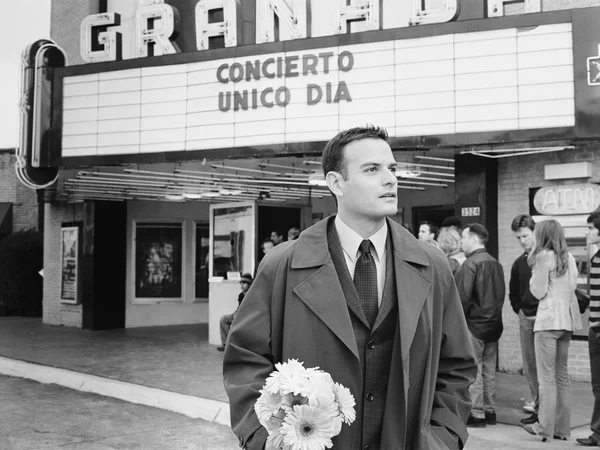 Man in suit with flowers waiting in front of movie theater