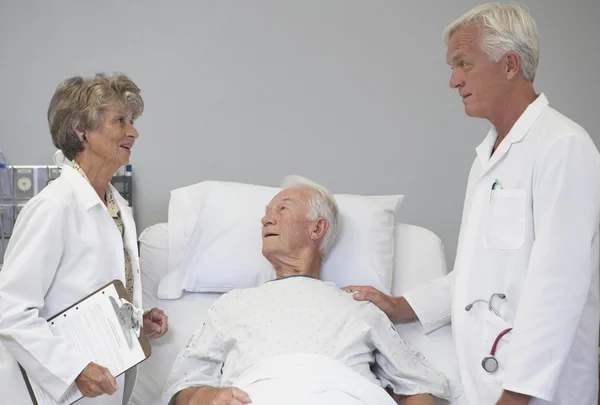 Male and female doctors talking with senior male patient in hospital bed