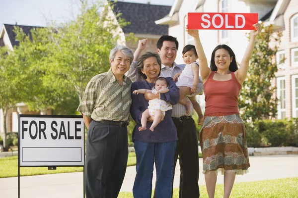 Multi-generational Asian family holding up Sold sign in front of house