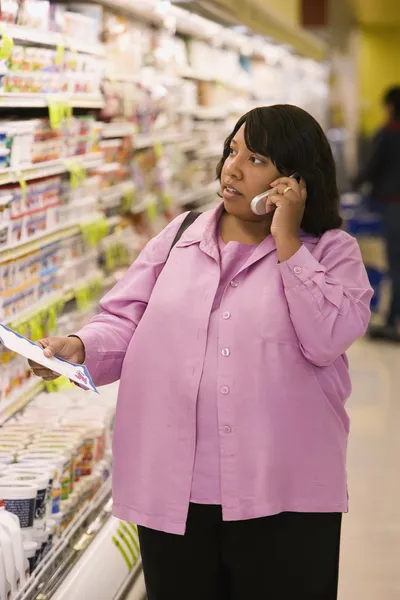 Woman on cell phone with grocery list in store