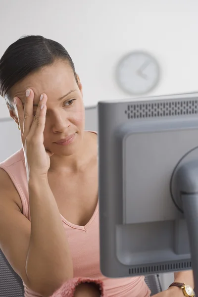 Frustrated woman looking at computer with hand on face