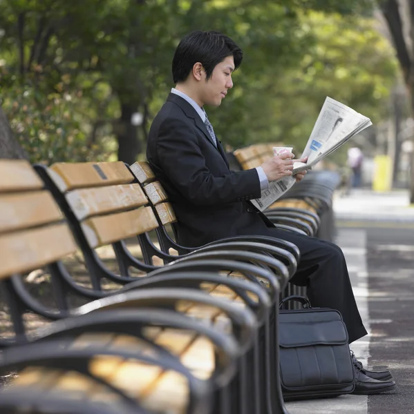 Asian businessman reading newspaper on park bench