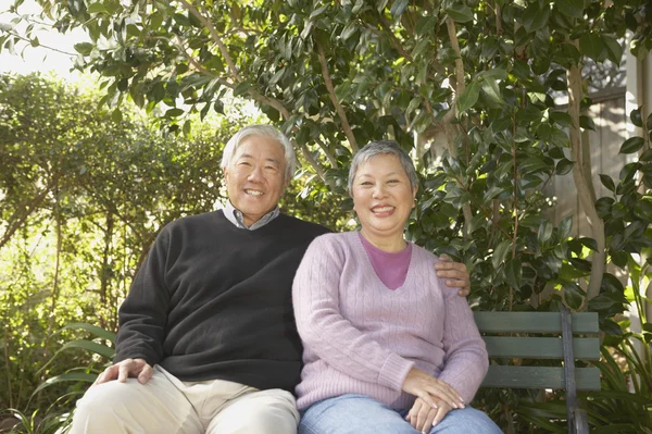 Senior Asian couple sitting on a park bench hugging