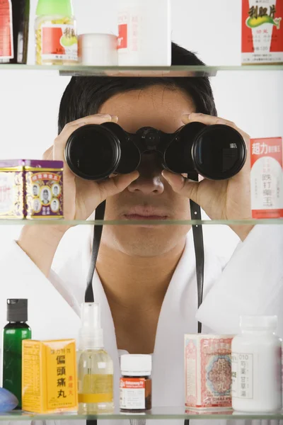 Asian man looking through binoculars at medicine cabinet