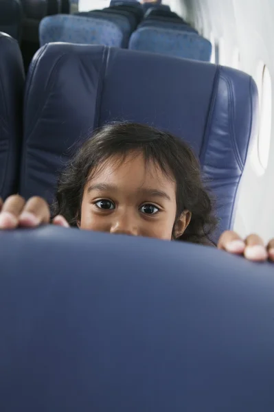 Portrait of young girl peeking over airplane seat