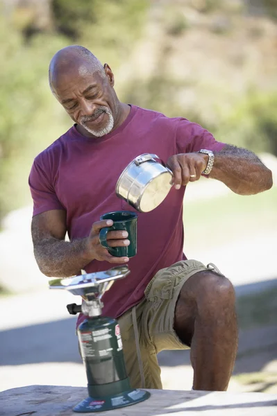 Middle-aged African American man pouring coffee from camp stove