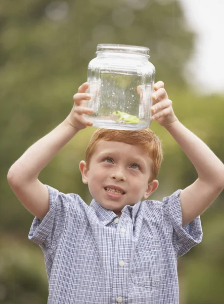 Young boy looking at frog in glass jar outdoors