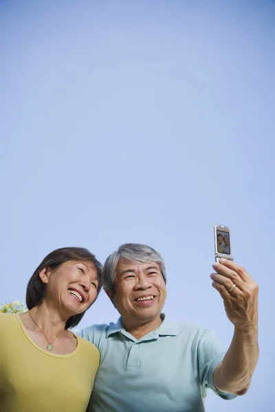 Senior Asian couple taking own photograph with cell phone