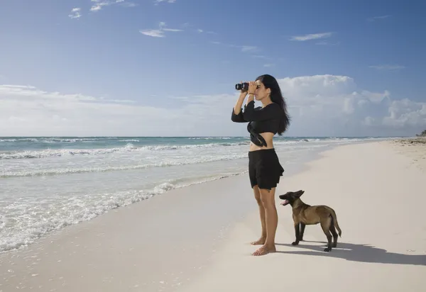 Hispanic woman using binoculars at beach