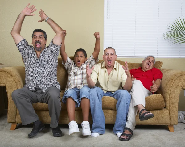 Multi-generational Hispanic male family members cheering on sofa