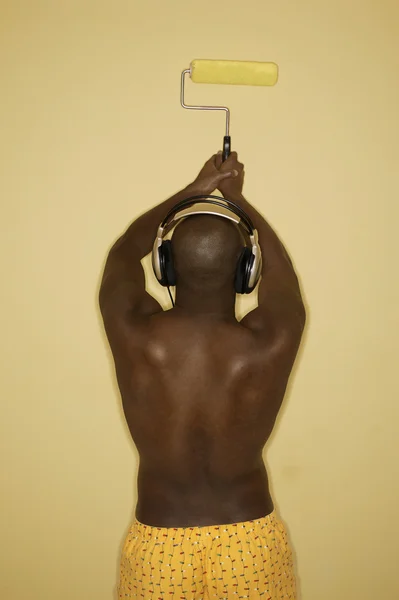 Rear view of man painting wall while listening to music