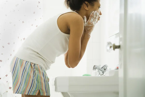 African woman washing face in bathroom sink