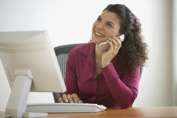Woman smiling while talking on the phone at desk with computer