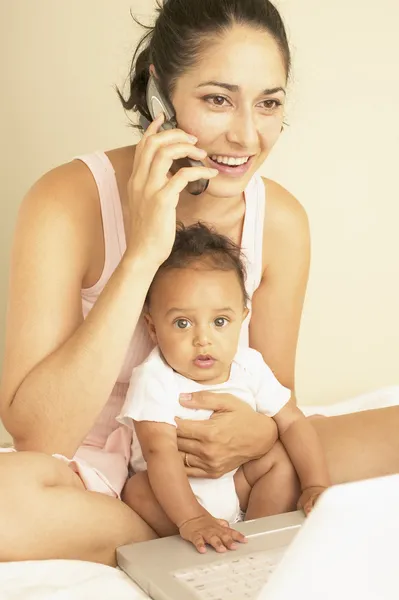 Young mother talking on phone with baby in arms