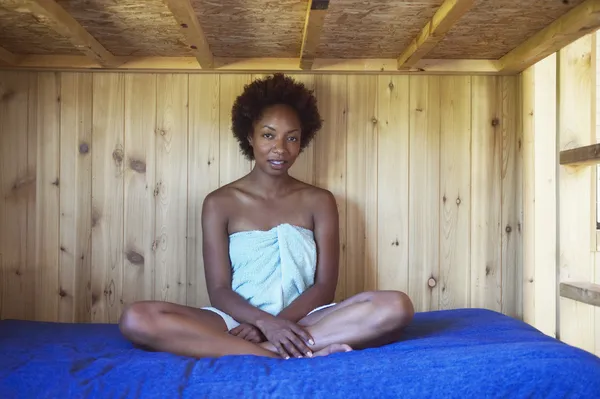 African American woman in towel sitting on wooden bunk