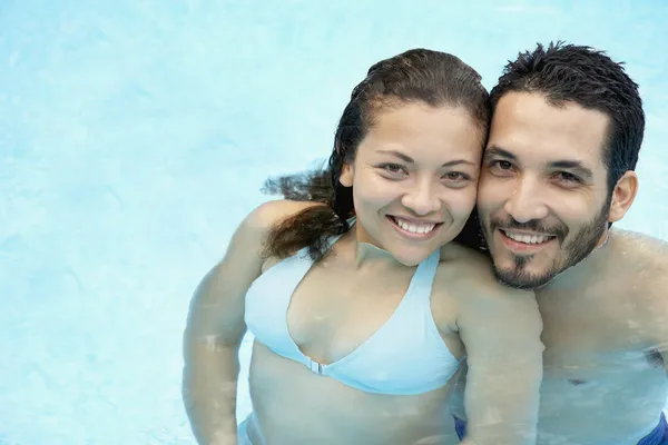 Hispanic couple hugging in swimming pool