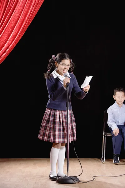 Hispanic girl reading from paper on stage