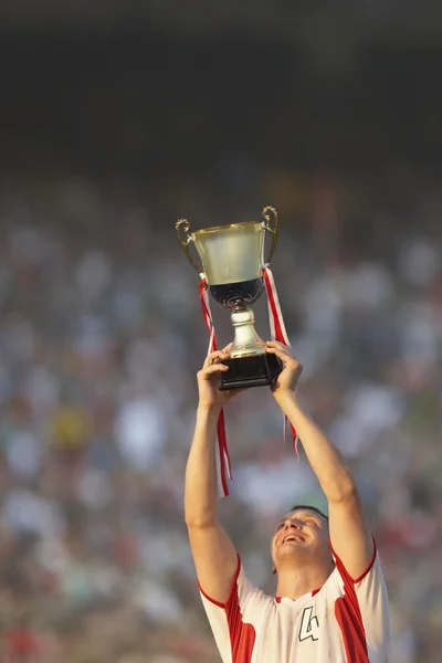 Male soccer player triumphantly holding up trophy