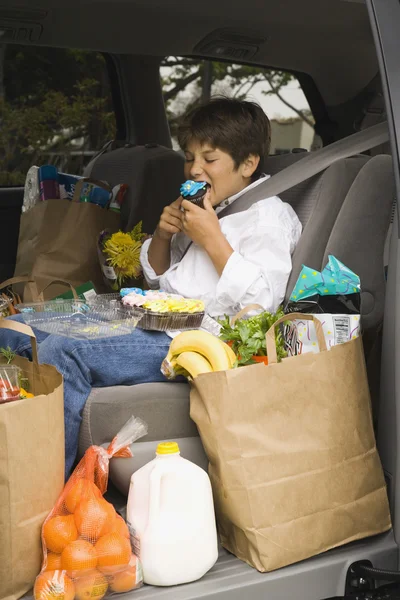 Boy sitting in backseat of car eating with groceries