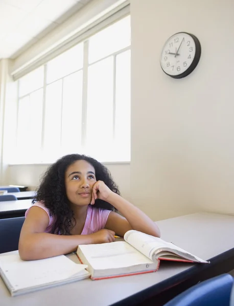 African girl day dreaming at desk in classroom