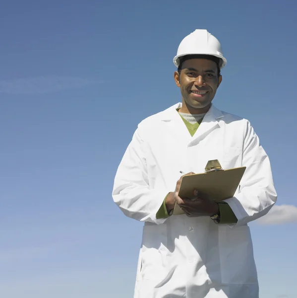 Man with hard hat and clipboard smiling outdoors