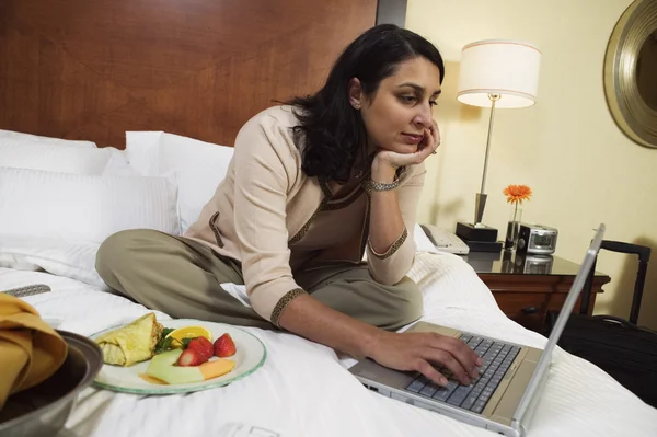 Businesswoman with laptop and food on hotel bed