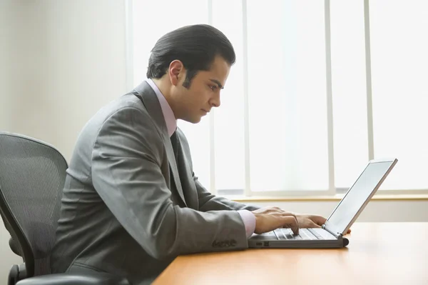 Profile of businessman sitting at desk working on laptop computer