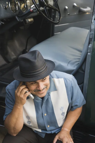 Middle-aged Hispanic man talking on cell phone in classic car