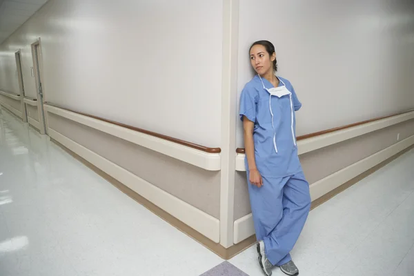 Hispanic female doctor leaning against wall at corner of corridor