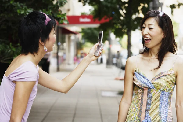 Woman photographing friend with camera phone